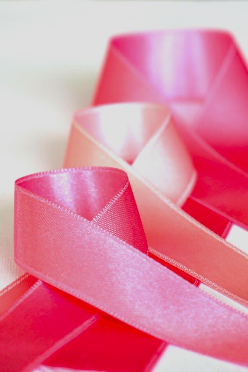 Three satin pink ribbons curled on white background to represent Vigilant Care For Women during breast cancer.