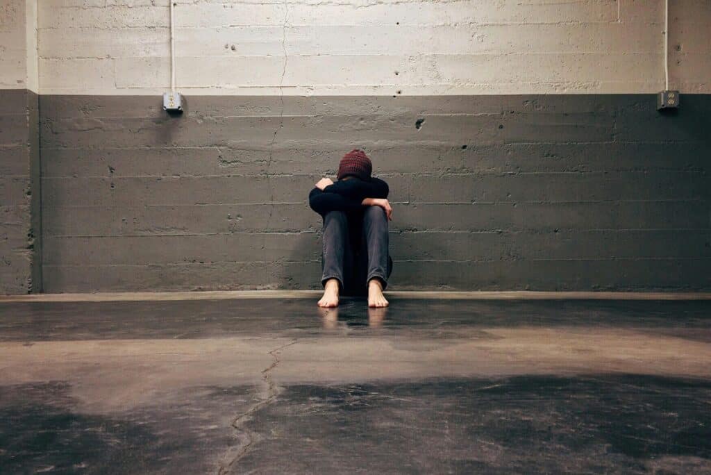 Person sitting alone against wall, symbolising distress, isolation, and Possible Predictors Of Suicide.