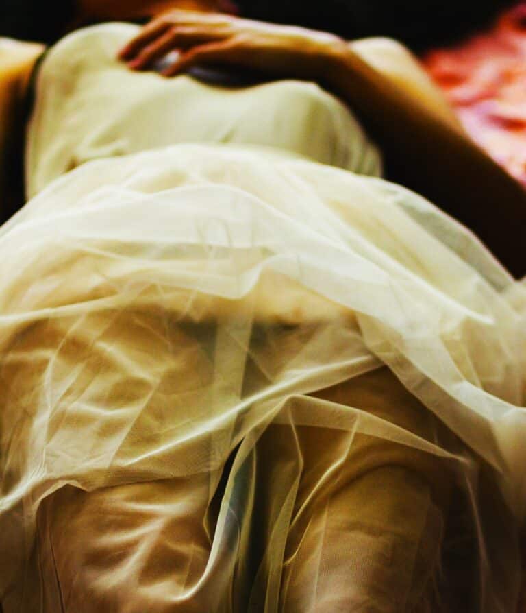 Person lying still under soft fabric, symbolising dissociation, freeze response, and Shutting Down Under Trauma.