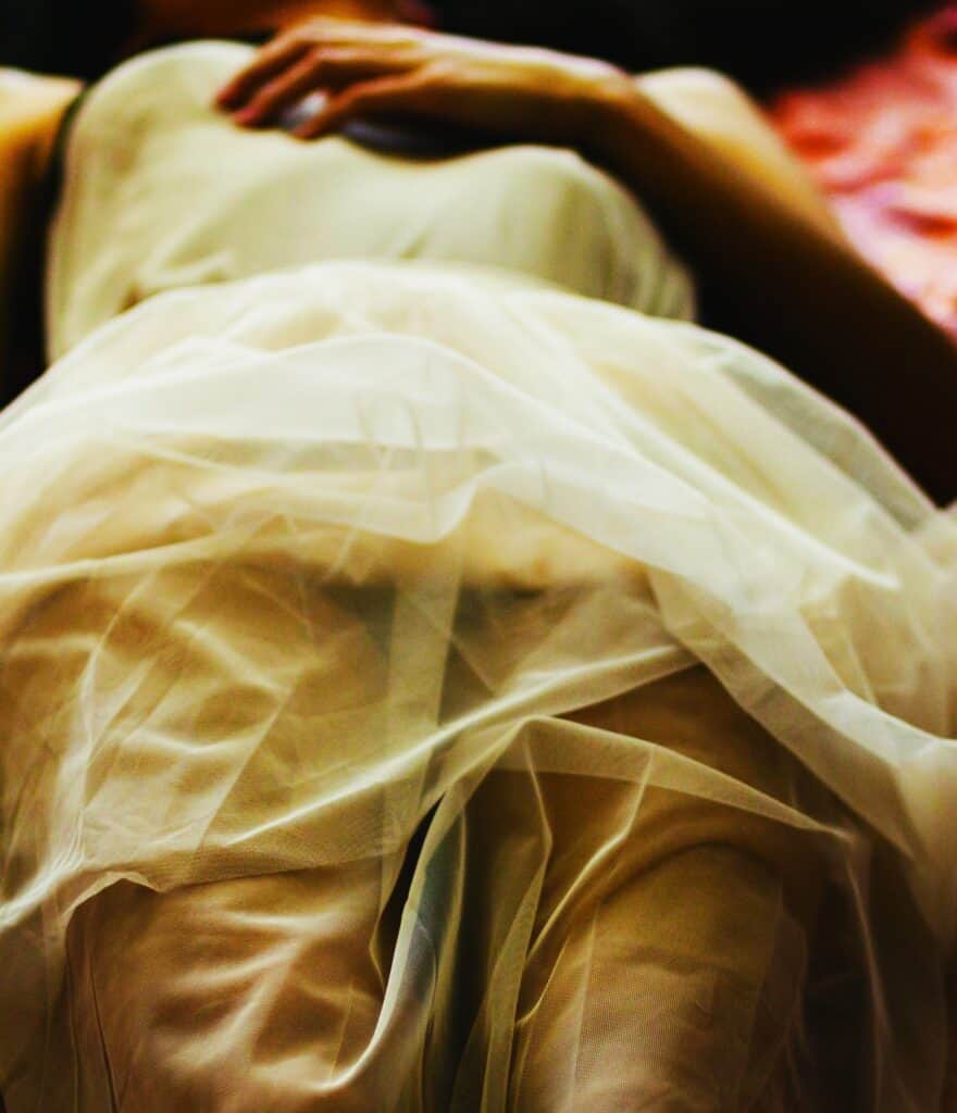 Person lying still under soft fabric, symbolising dissociation, freeze response, and Shutting Down Under Trauma.