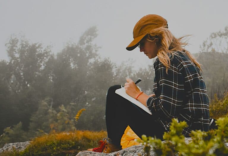 A woman journalling alone outdoors to process emotions and grow resilient by Viewing Vulnerability Differently.
