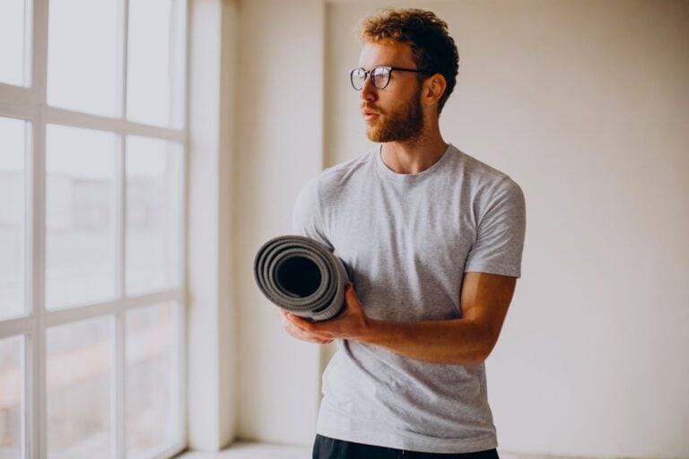 Man holding exercise mat indoors, preparing for a gym-free routine as an alternative and using Zero Gym Workout Ideas.