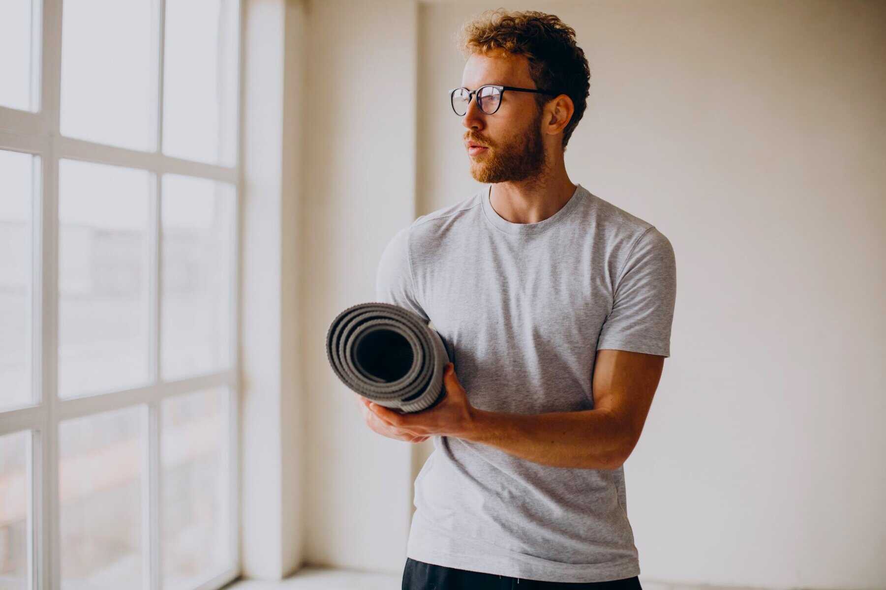 Man holding exercise mat indoors, preparing for a gym-free routine as an alternative and using Zero Gym Workout Ideas.