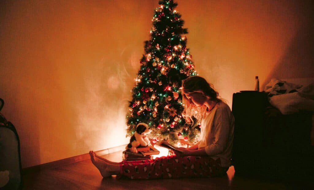 Young girl reading near Christmas tree, expressing why Holiday Kindness Matters in uplifting and quiet moments.