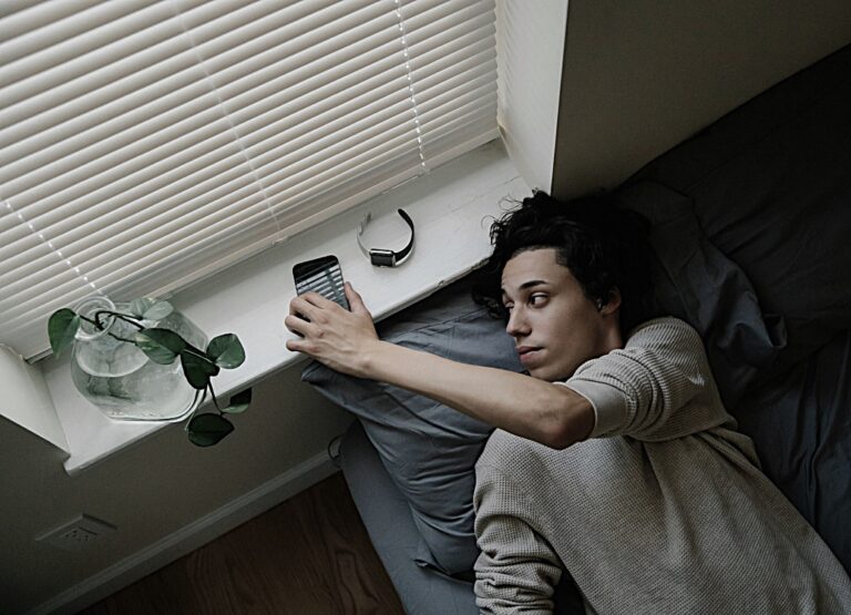 Person in bed scrolling on phone before sleep, illustrating the need for a Calming Nighttime Ritual.
