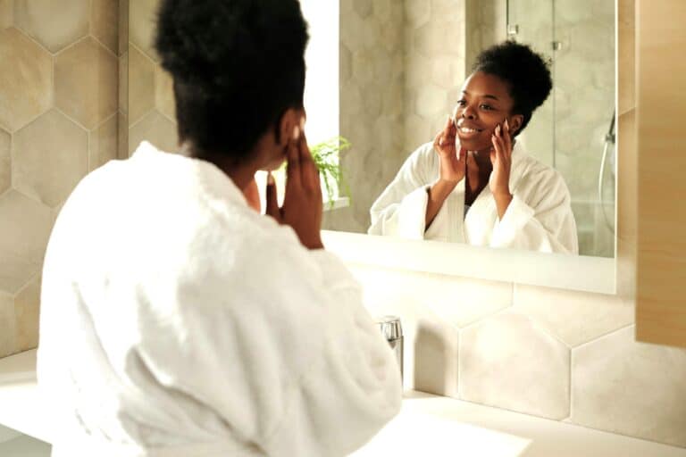 Woman in robe smiling at reflection, symbolising self-awareness, emotional safety, Trust And Emotional Regulation.