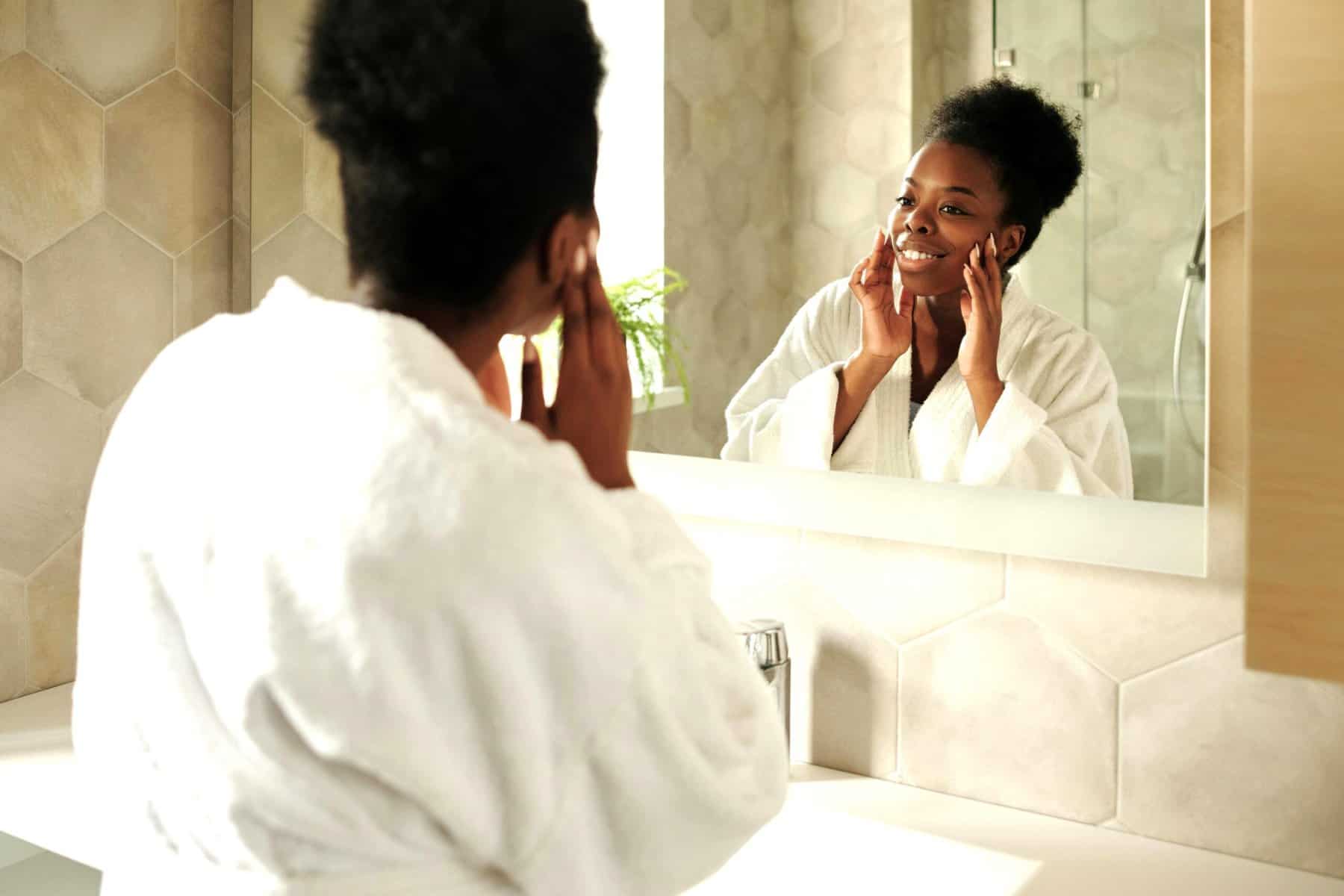 Woman in robe smiling at reflection, symbolising self-awareness, emotional safety, Trust And Emotional Regulation.