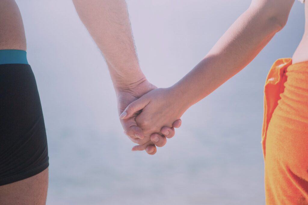 Couple holding hands near water, symbolising trust, healing, and Judging Romantic Journeys after vulnerability.