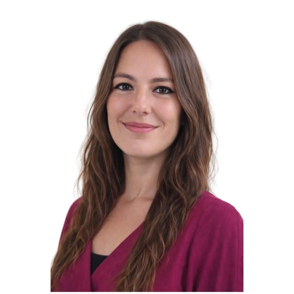 A professional woman with long brown hair smiling gently, dressed in a magenta blazer, against a plain white background, conveying warmth and approachability.