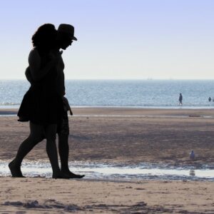 Silhouetted couple walking closely together on the beach during sunset, symbolising connection and emotional intimacy.