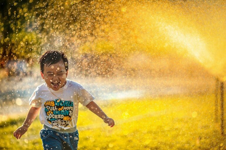 A young boy runs through water sprinklers outdoors